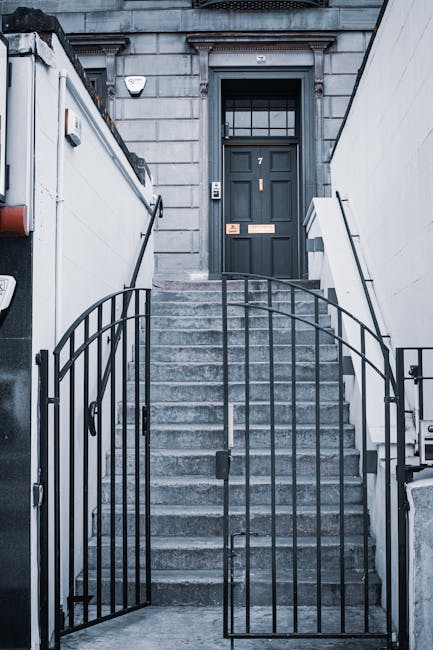 A set of concrete stairs leading up to a dark grey, wooden front door with a glass-paneled section and brass mailbox slot, situated at the entrance of a Clapham flat. The staircase is flanked by white
